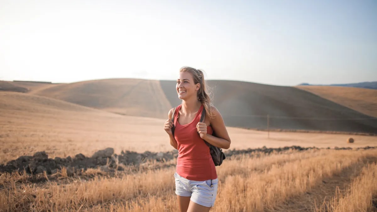 Smiling woman in casual attire enjoying a summer hike through golden fields at sunset.